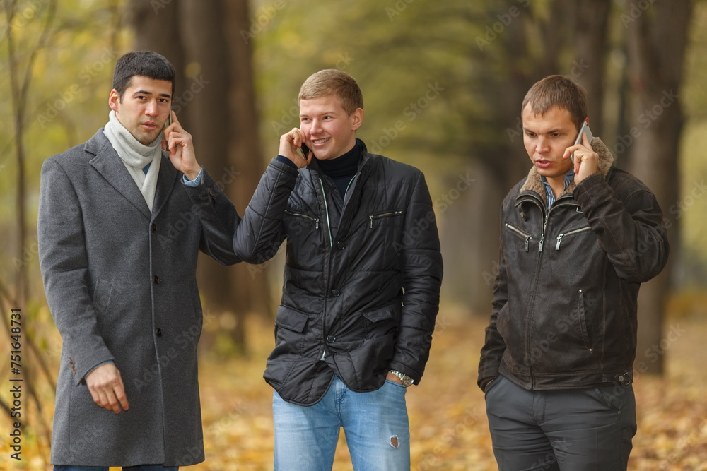 Half growth portrait of three young men in autumn park talking on phone Half growth portrait of three young men in autumn park talking on phone