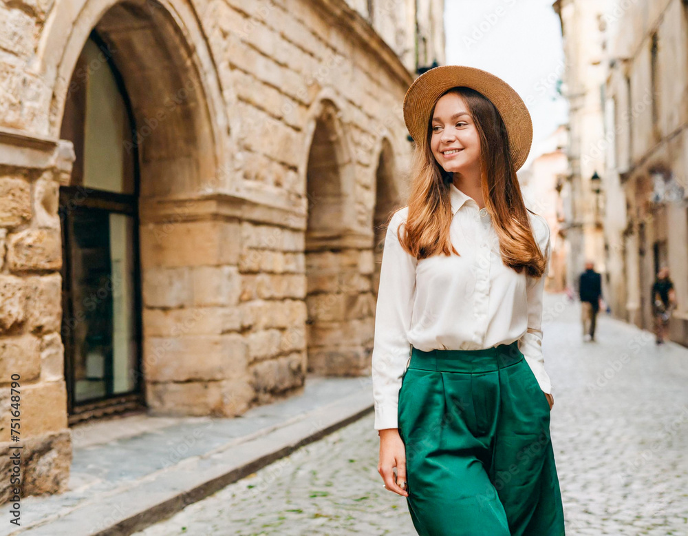 young slim girl dressed in wide green trousers and hat in old european city