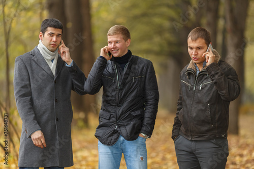 Half growth portrait of three young men in autumn park talking on phone