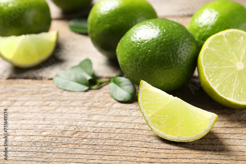 Whole and cut fresh limes on wooden table. Space for text