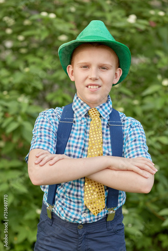 Boy in hat with arms folded on chest against green bushes photo