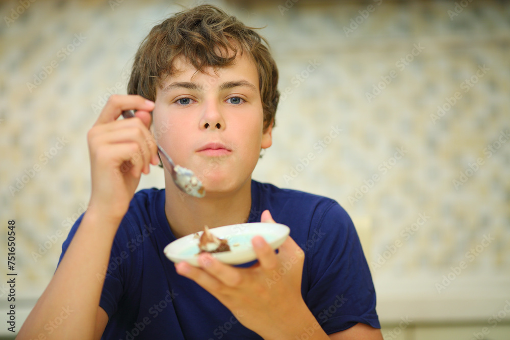 Happy boy teen eats confection from saucer in kitchen, shallow dof Happy boy teen eats confection from saucer in kitchen, shallow dof
