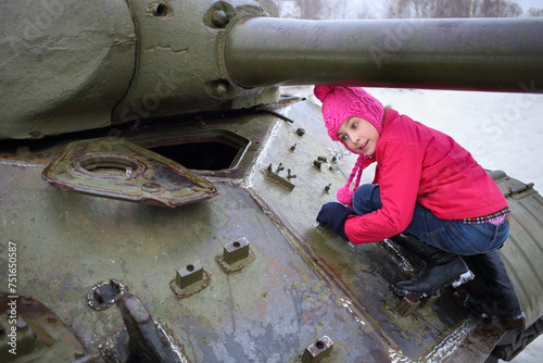 Girl in a pink jacket and hat climbed on the Soviet tank photo