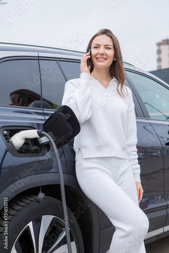 Young woman charging her electric car at a charging station in the city. Eco fuel concept. The concept of environmentally friendly transport. Recharging battery from charging station. © romeof