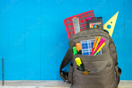 Backpack with different colorful stationery on table. Blue background. Back to school.