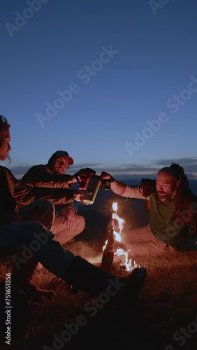 As the last light of day lingers on the horizon, a group of friends gathers around the warmth of a campfire. The sky, painted in shades of twilight, provides a serene backdrop. Two of the companions