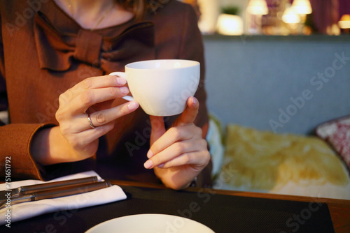Closeup of female hands holding white cup of tea above table in restaurant
