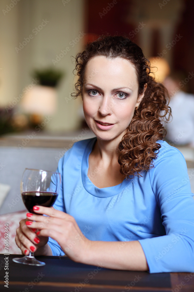 Woman in blue dress holds glass of red wine in restaurant, shallow dof Woman in blue dress holds glass of red wine in restaurant, shallow dof
