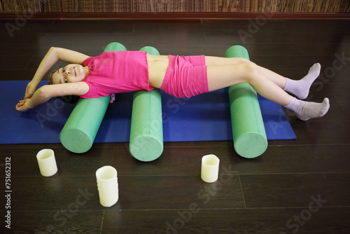 Girl childs smiles and does exercise on three rollers on floor near candles