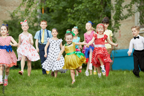 Group of eleven children dressed in dance suits runs across grassy lawn photo