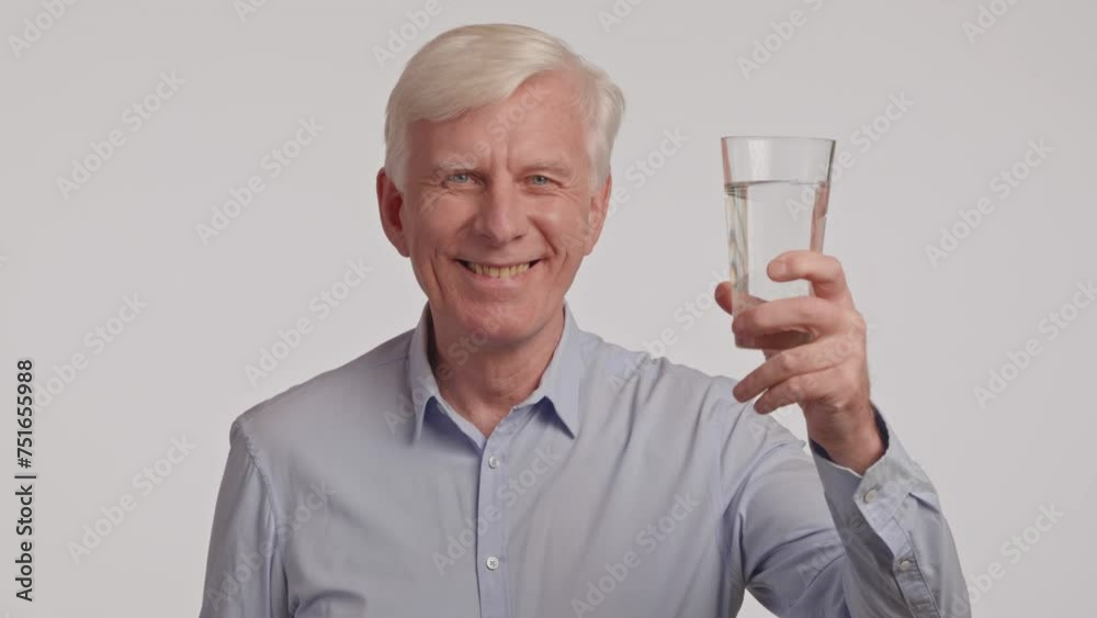 An elderly man is holding a glass of water with a smile on his face An elderly man is holding a glass of water with a smile on his face