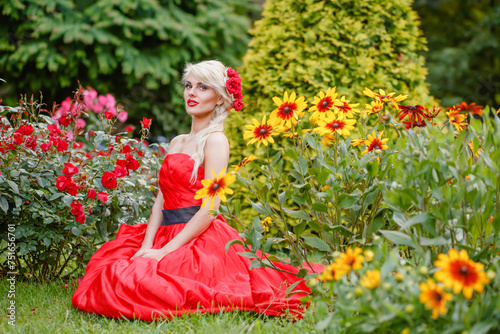 Half length portrait of beautiful woman in red dress in summer park sitting on grass among flowers