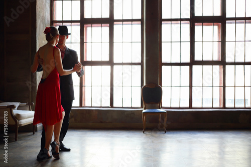 Woman in red dress and man in black suit dance tango near window