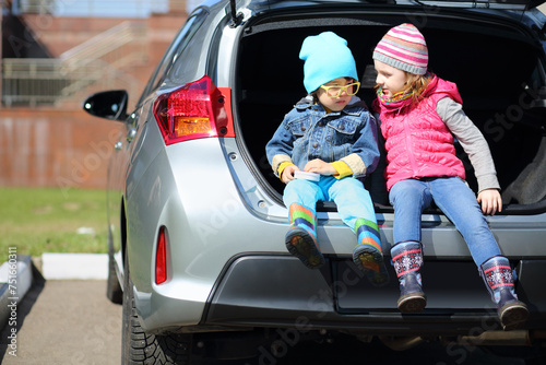 Little boy in yellow glasses and girl sitting in open trunk of foreign car