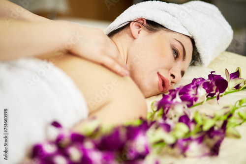 Female massage therapist hands massage neck of woman lies on couch with flowers in beauty salon.