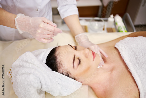 Beautician hands in rubber gloves and woman covered by towel that lies on couch in beauty salon.