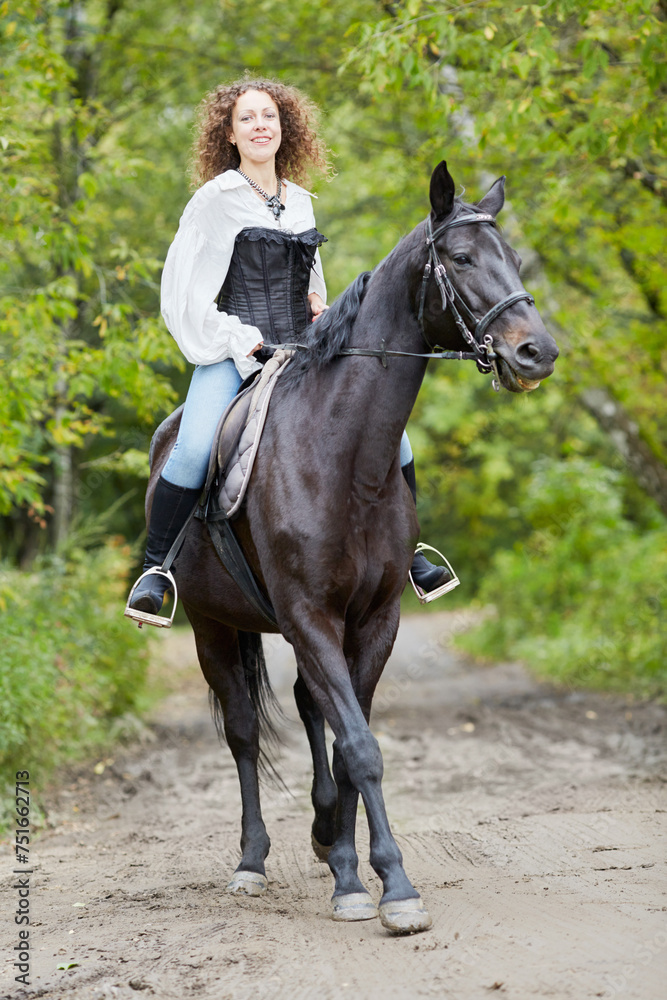 Smiling woman with curly hair rides on bay horse in the park Smiling woman with curly hair rides on bay horse in the park