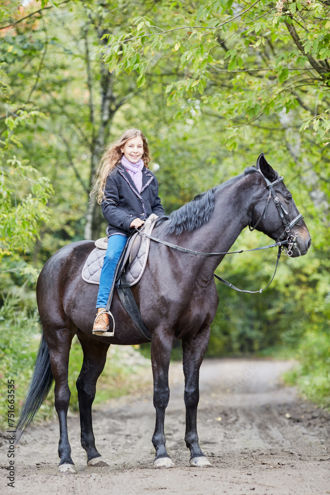 Smiling teenage girl sits on chestnut horse in park Smiling teenage girl sits on chestnut horse in park