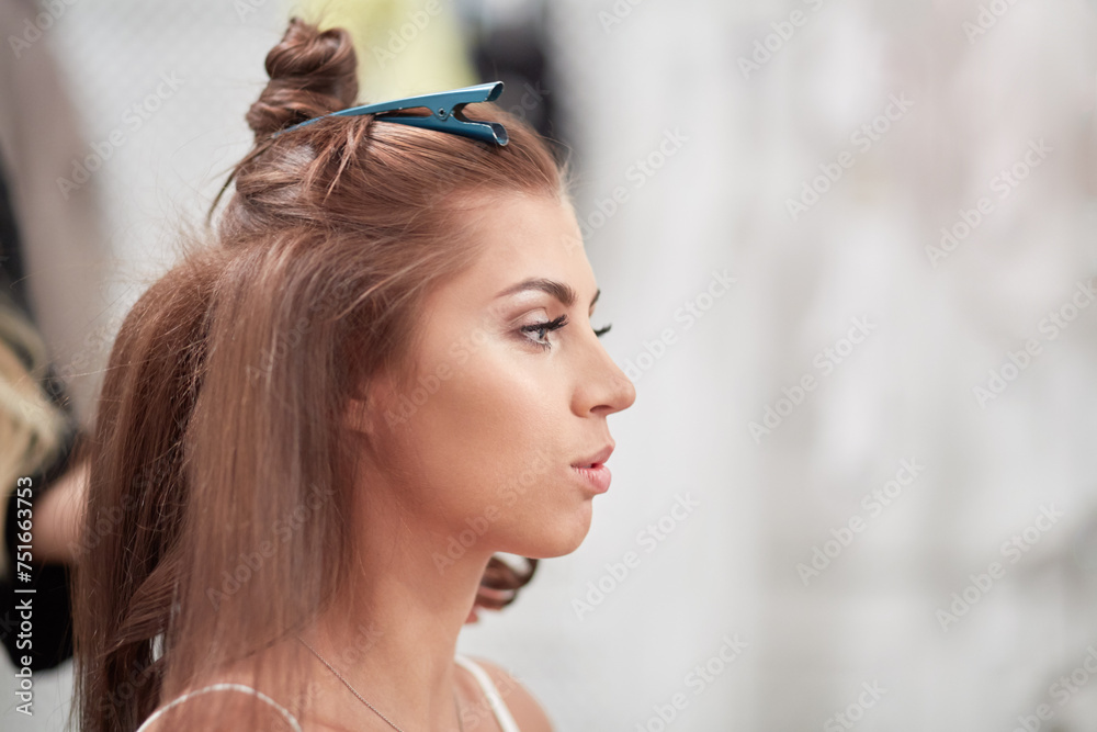 Naklejka premium Head in profile of young woman while visagist makes hairdo.