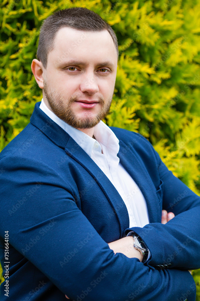 Unshaven handsome man in blue jacket poses in green summer garden Unshaven handsome man in blue jacket poses in green summer garden