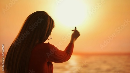Silhouette of a woman making a Korean heart sign with her fingers at sunset