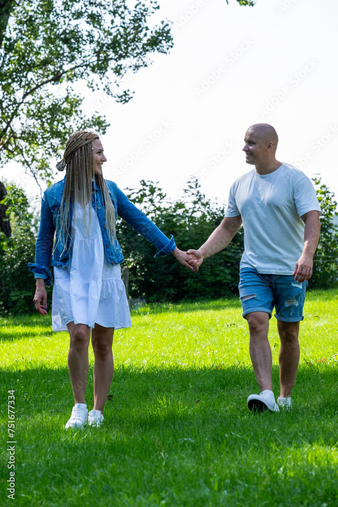 A smiling couple walks hand in hand in a sunny park, exuding warmth and connection. The image evokes themes of love, companionship, and outdoor leisure