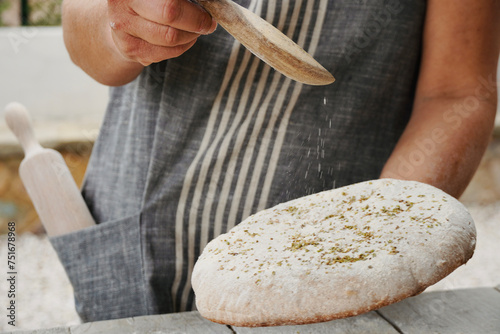 Fototapeta Naklejka Na Ścianę i Meble -  Bread maker with apron sprinkles spices on top of the bread dough.