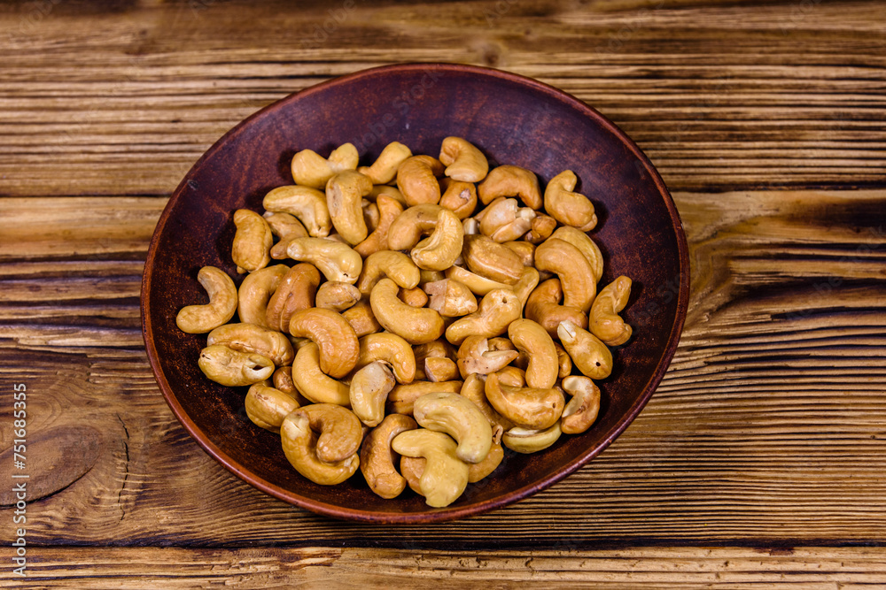 Ceramic plate with roasted cashew nuts on a wooden table Ceramic plate with roasted cashew nuts on a wooden table