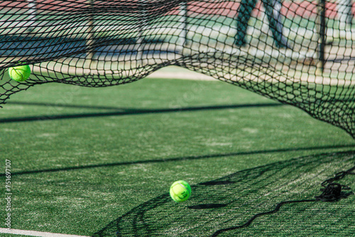 Two tennis or padel  balls on a vibrant green court with a net casting intricate shadows, highlighting the dynamic and aesthetic elements of the sport.