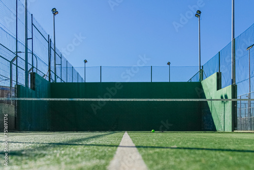Empty paddle court, green walls, blue sky, and a resting ball