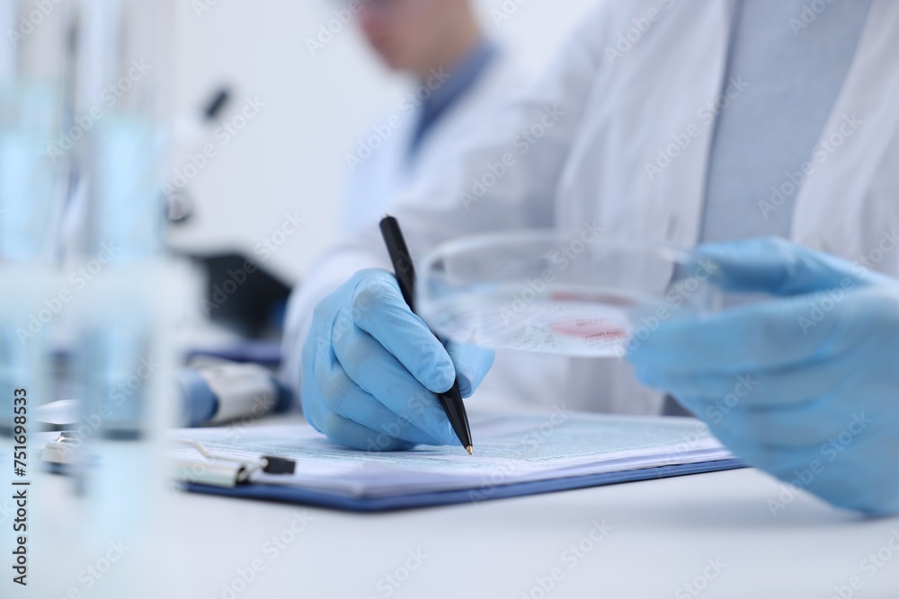 © New Africa - Laboratory worker holding petri dish with blood sample while working at white table, closeup