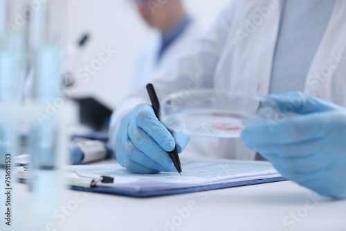 Laboratory worker holding petri dish with blood sample while working at white table, closeup