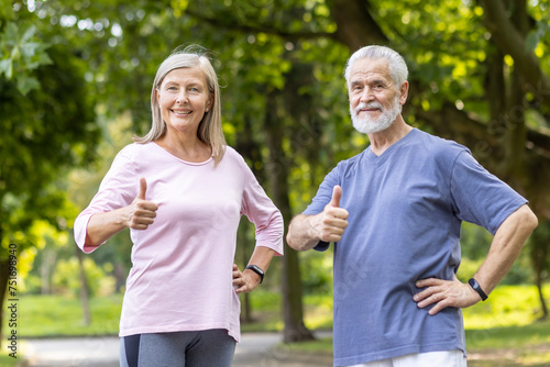 Portrait of energetic and active man and woman, senior couple standing in park in sportswear, looking at camera and showing super gesture with fingers.