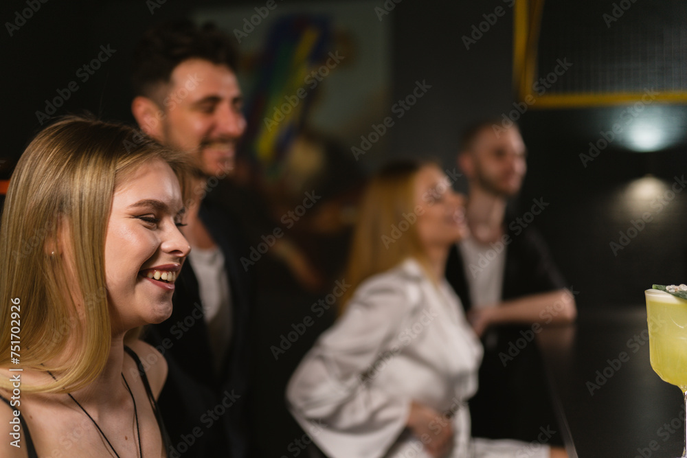 Group of young cheerful people chill in establishment. Ladies and gentlemen have drinks while talking sitting at bar counter