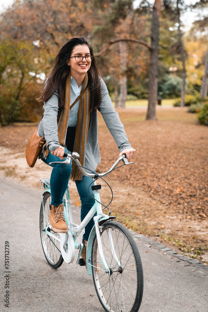 Cheerful young female prentice riding a bicycle in city park while rushing to work in her new company. Happy woman enjoying outdoors.