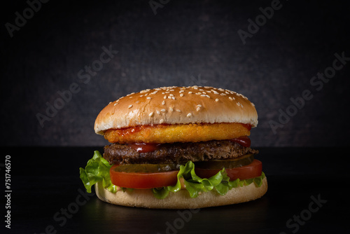 fresh burger with sesame bun, beef patty and vegetables on a dark background with a gradient spot of light. moody photo with copy space. side view