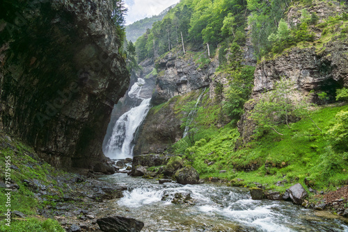 A view of a majestic waterfall carving through the Ordesa Valley, embraced by lush cliffs and vibrant greenery photo