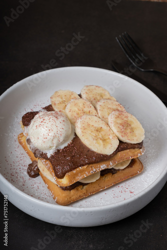 Belgian waffles with bananas and chocolate sauce with ice cream angle view