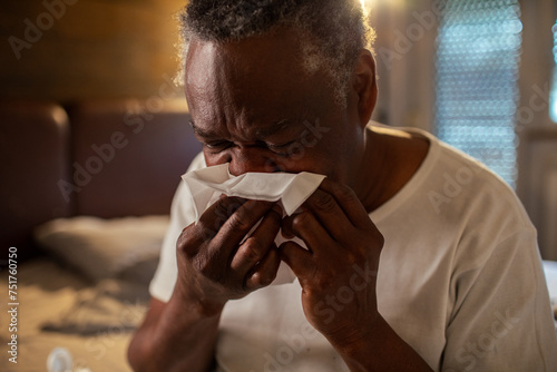 Senior man blowing nose in paper tissue in bedroom photo