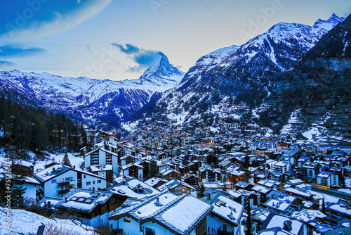 Aerial view of the village of Zermatt overlooked by the Matterhorn peak in the Swiss Alps in winter - Sunset over wooden chalets surrounded by snow capped mountains