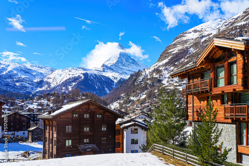 Wooden chalets in the village of Zermatt overlooked by the Matterhorn peak in the Swiss Alps in winter - Idyllic landscape surrounded by snow capped mountains