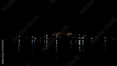 July 7, 2021 - Nile River, Luxor Egypt. The dark water reflects the illuminated mountain and buildings on the West Bank of Luxor as the small boat crosses the Nile River.