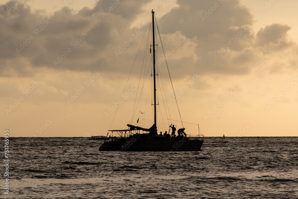 backlighting of boat at sunset on the beach in Cartagena, Colombia while people stroll and enjoy the scenery