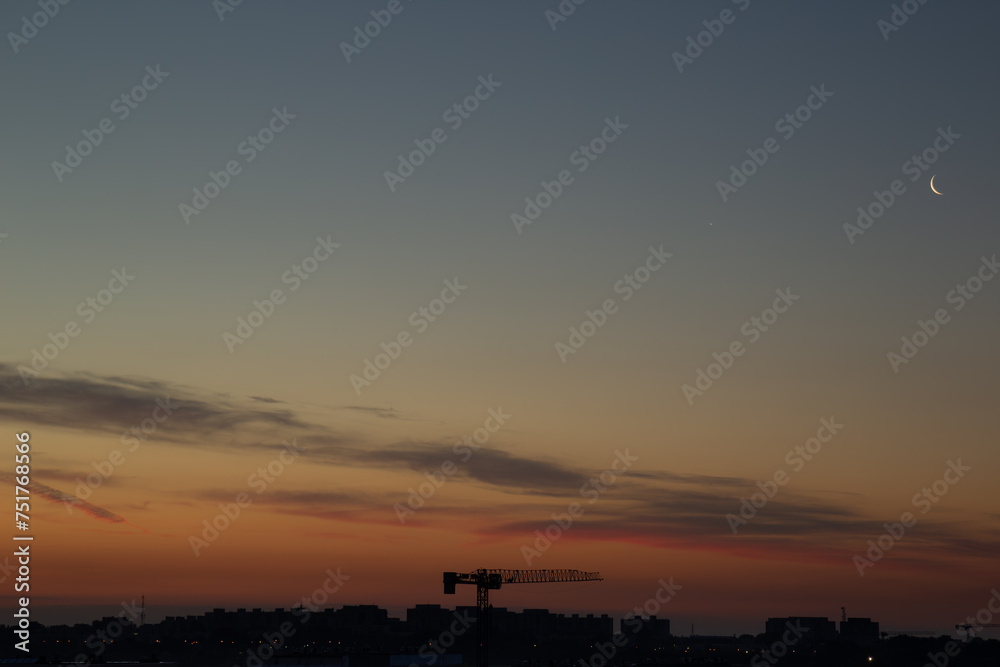 Sunrise over the city with the moon and crane against the background of the colorful sky