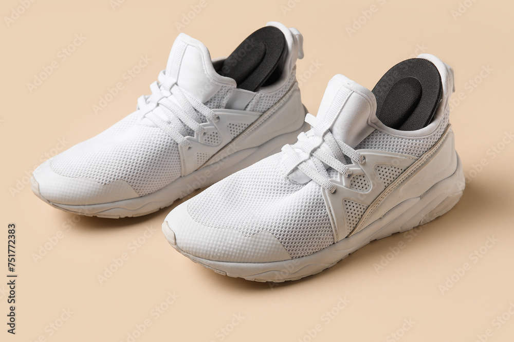 Pair of stylish white sneakers with black orthopedic insoles on beige background Pair of stylish white sneakers with black orthopedic insoles on beige background