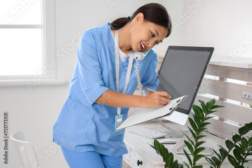 Female Asian medical intern talking by telephone in clinic