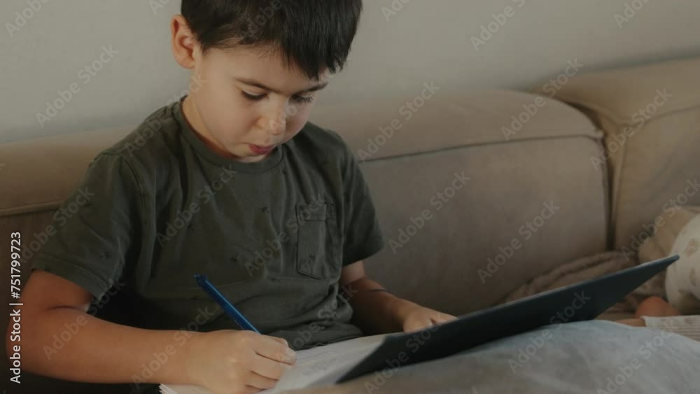 Adorable boy, sitting on the sofa, writing in notebook with pen within the cozy comfort of his home living-room. Adorable boy, sitting on the sofa, writing in notebook with pen within the cozy comfort of his home living-room.