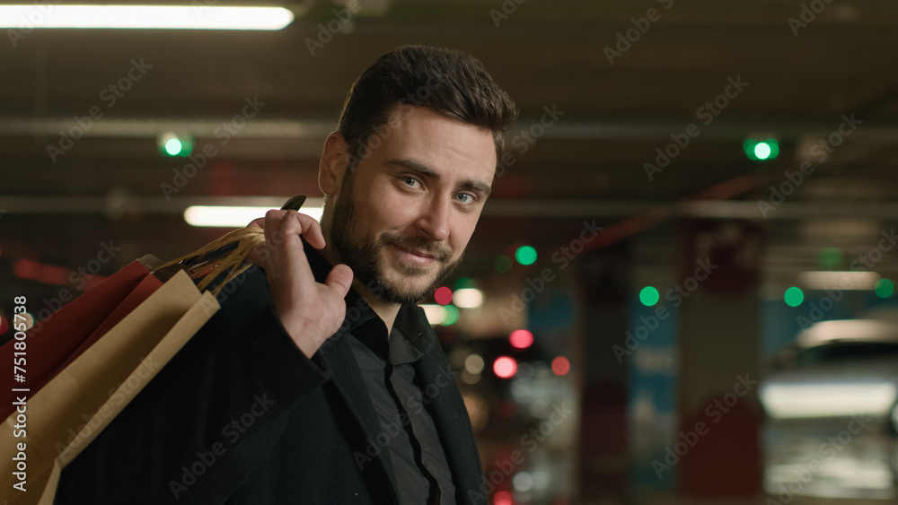 Naklejka premium Caucasian man shopper guy customer businessman stand in underground car parking carry shopping bags from shop mall supermarket buy presents gifts happy joyful tourist hold purchases sale black friday