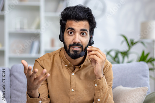 Photography Enthusiastic latino male wearing professional headset with microphone and gesturing to camera during video call