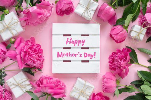 Fototapeta Naklejka Na Ścianę i Meble -  Bouquet of beautiful pink peonies with gift boxes in paper wrapping. Round frame of flowers. White wooden board with text Happy Mother's Day!